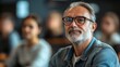 © liliyabatyrova - A thoughtful man with silver hair and glasses participates in a dynamic classroom discussion, surrounded by attentive peers. His expression reflects confidence and curiosity