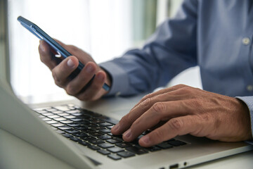 Wall Mural - Closeup man hands using smartphone and laptop. Businessman works with computer and mobile phone