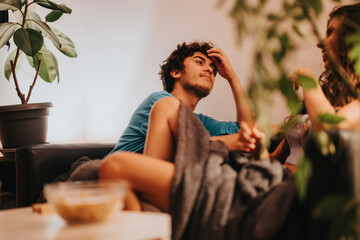 Wall Mural - A young couple enjoys a casual moment on their couch, surrounded by indoor plants, creating a cozy and relaxed atmosphere. The scene captures tranquility and domestic comfort.