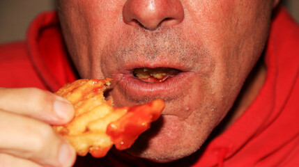 Wall Mural - A man biting a waffle fry with ketchup while eating in a restaurant.