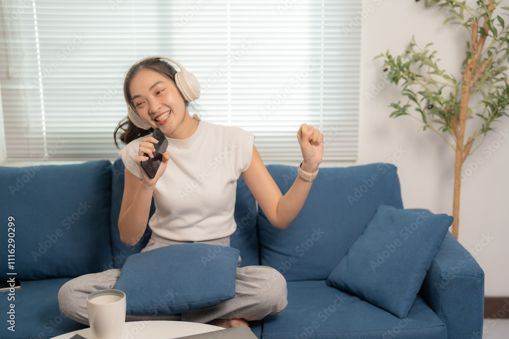 Sitting on a blue sofa in a living room, a young asian woman enjoys ...