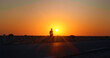 © RecCameraStock - Man walking along the road with a sun set in the background. Sunset light in the dark and a man silhouette having a walk in sahara.