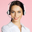 © vgstudio - Call center help line service. Studio portrait image of customer support phone sales operator in headphones, isolated pink color background. Happy smile business woman. Caller telecom worker. Square