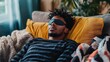 © Suphawan - A man relaxing on a couch, wearing a contoured eye mask, surrounded by soft throw blankets