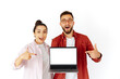 © Kateryna - Excited man and woman of arabian or caucasian ethnicity, holding a laptop with a blank mockup screen, both smiling and pointing at it, promoting content or product, stand on isolated white background