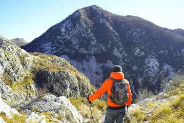 Wall Mural - Tourist enjoying the view in the mountains. Photographed from behind, a man with a backpack stands against the backdrop of a beautiful mountain landscape in the Orjen Nature Park near Herceg Novi