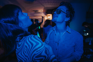 Poster - A vibrant scene of young adults having fun at a neon-themed birthday party. The blue lighting creates a lively and energetic atmosphere, highlighting the joy and excitement of the celebration.