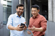 © Liubomir - Two colleagues share a joyful moment outside, interacting with a smartphone and tablet. The scene captures a friendly, energetic vibe highlighting modern technology and communication.