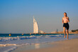 © khmelev - Woman running in summer. Fitness woman running by the beach at sunrise. Healthy active lifestyle girl exercising outdoors. Dubai. UAE. Burj Al Arab Jumeirah.