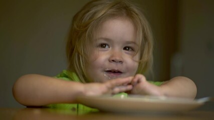 Wall Mural - Baby eats with a spoon. Child have a meal. Little kid eating kids food. Baby porridge. Little baby eating healthy food of dishes. A cute fun baby eating her dinner. Kids facial expression.