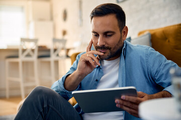 Wall Mural - Smiling man surfing the net on touchpad while relaxing at home.