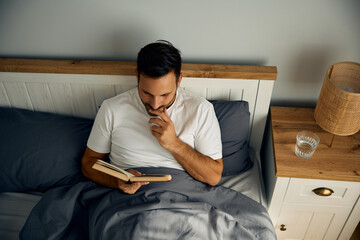 Wall Mural - Above view of man reading book in bed.