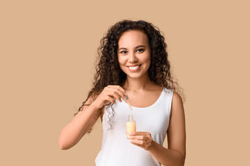 Canvas Print - Beautiful young African-American woman with bottle of face serum on beige background