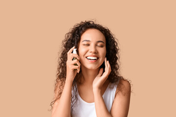 Canvas Print - Beautiful young African-American woman applying cosmetic oil on face against beige background