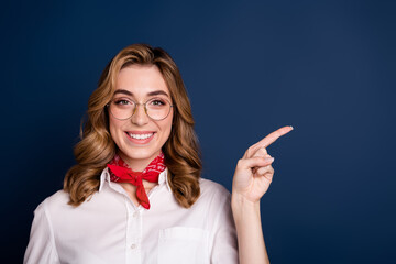 Wall Mural - Charming young woman in stylish outfit smiling and pointing on dark blue background