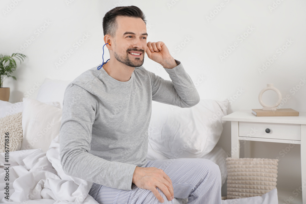 Handsome man putting earplugs in bedroom