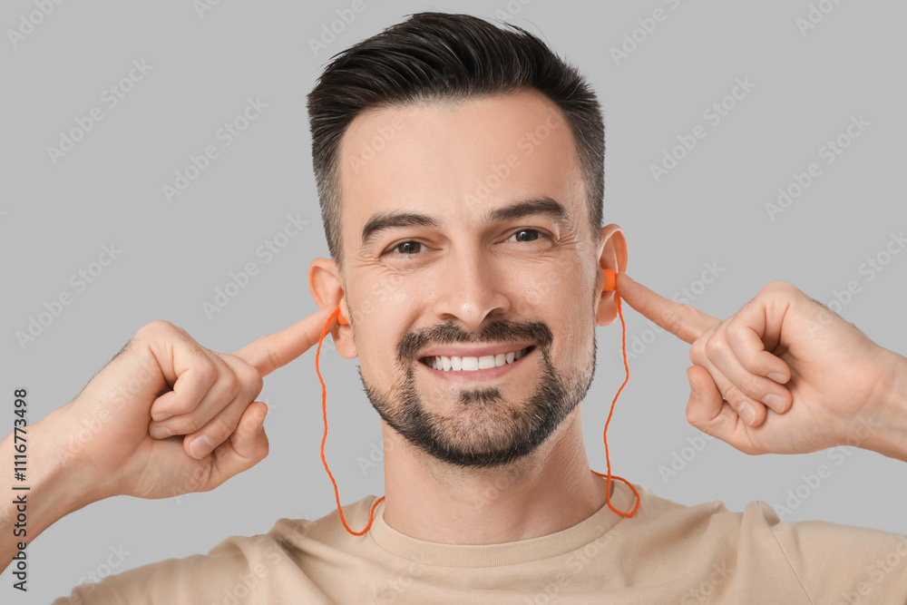 Handsome man with earplugs on grey background, closeup
