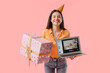 © Pixel-Shot - Happy young woman in party hat with laptop and gift celebrating Birthday online on pink background