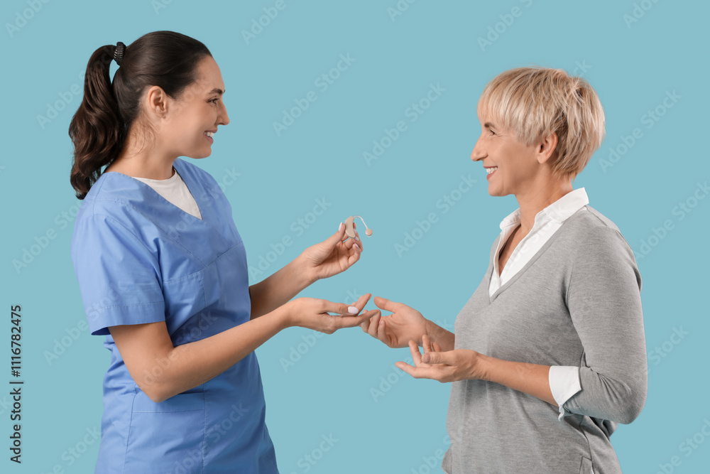 Doctor explaining mature woman how to use hearing aid on blue background