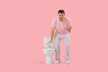 Wall Mural - Suffering man near toilet bowl with paper pin on pink background. Hemorrhoid concept