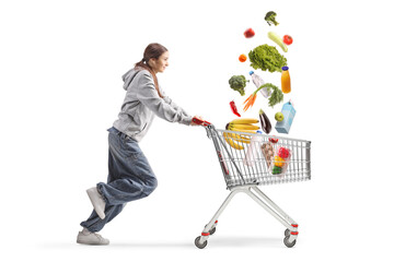 Teenage girl running with falling groceries in a shopping cart