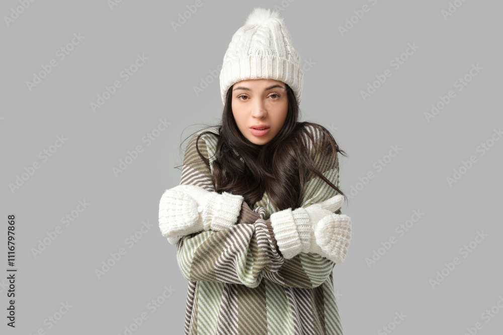 Frozen young woman in winter clothes on grey background