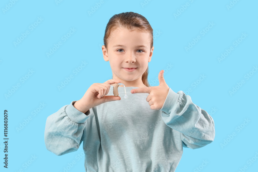 Little girl pointing at hearing aid on blue background