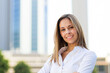 © Minerva Studio - Businesswoman smiling with folded arms in front of office buildings