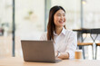 © David - Portrait of a business asian woman sitting in an office with her colleagues in the background. Happy business woman working in a co-working office.