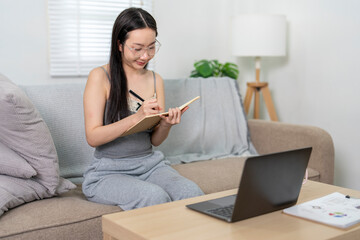 Young woman taking notes while studying online at home