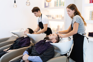 Wall Mural - Young female hairdresser stylist washing hair of young male client in beauty salon