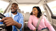 © Prostock-studio - Enjoying Travel Concept. Smiling African American man driving modern luxury car, happy young woman sitting on the front passenger seat, looking on the driver, family going on roadtrip, windshield view
