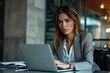 © Luisa - A woman working on her laptop at a desk in an office environment, concentrating on the screen. Modern and professional setting.