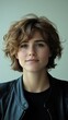 © JO BLA CO - A young woman with short, curly hair stands confidently in front of a pale background. She wears a black leather jacket over a simple top, showcasing a relaxed demeanor