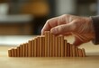 © Bambalino Studio - A person is placing wooden blocks on top of each other, creating a tall stack. The blocks are arranged in a way that they seem to be falling, as if they are about to topple over