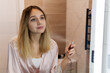 © diy13 - A blonde girl in a pink bathrobe is sprayed with perfume in the bathroom. Beautiful young woman using deodorant at home