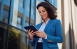 © Pixora Labs - Businesswoman wearing blue coat holding a tablet, office building in the background