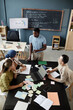 © Seventyfour - Vertical shot of young African American teacher standing at desk talking to students explaining task, during speaking club session in English language school for adult learners