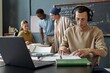 © Seventyfour - Medium shot of concentrated multiracial man in headphones completing listening task sitting at desk in classroom of language school for adult learners, copy space