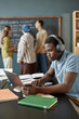 © Seventyfour - Vertical shot of African American male student typing on laptop keyboard completing test task while listening to audio in headphones in English class at language school for adult learners, copy space