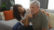 © Krakenimages.com - Middle-aged couple sitting on a couch in their living room, the woman providing comfort to the man, highlighting a moment of love, empathy, and relationship support.