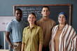 © Seventyfour - Portrait of diverse team of four smiling adult English teachers posing against blackboard in classroom of language school