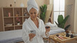 © Krakenimages.com - Mature woman relaxing indoors at a spa holding a glass of wine and looking at her phone wearing a bathrobe