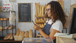 © Krakenimages.com - Woman in bakery wearing an apron uses smartphone surrounded by fresh bread and pastries, showcasing a cozy interior and her concentration on the business activities.