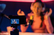 © Summit Art Creations - Selective focus camera screen in host channel of beautiful Asian listening the music on social media with listener, wearing pastel headphones on blurred background using mic at neon studio. Stratagem.