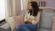 © Krakenimages.com - Woman sitting on a sofa with crossed arms in a cozy living room, featuring pillows, books, and a desk in the background