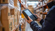 © Alex Alex - A man is holding a device for scanning barcodes or RFID tags. He works in a warehouse or in a logistics company. The background is shelving with stacks of packaged goods.