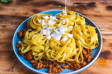 Wall Mural - Spaghetti Bolognese pasta nests with Bechamel sauce and minced beef fried with tomatoes, onions and carrots on a blue plate on a wooden table. Top view. Copyspace or space for text.