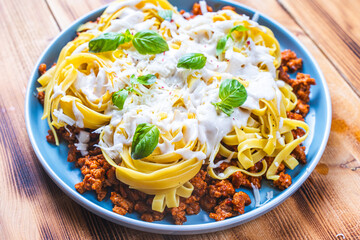 Wall Mural - Spaghetti Bolognese pasta nests with Bechamel sauce and minced beef fried with tomatoes, onions and carrots on a blue plate on a wooden table. Top view. Copyspace or space for text.