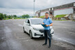 © Odua Images - A man confidently stands by his sleek car, holding an important document in an open area
